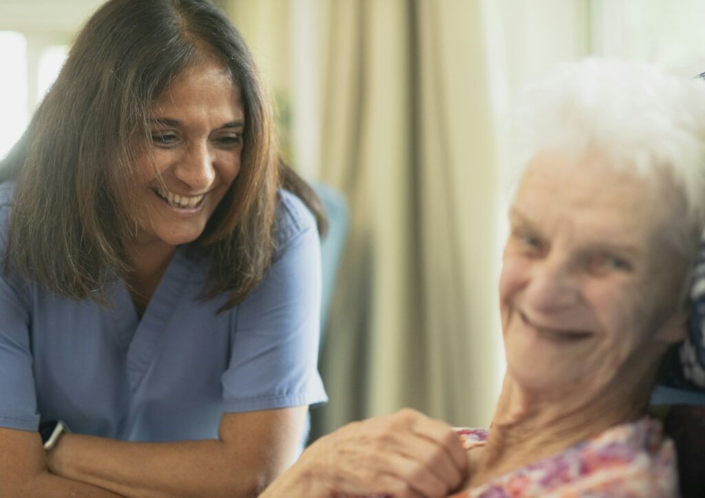 Smiling nurse with an elderly patient in a room, reflecting the work of a care assistant