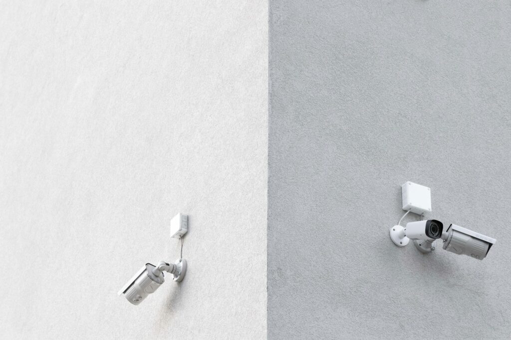 Three white CCTV cameras mounted on a building wall, the kind that need regular maintenance checks