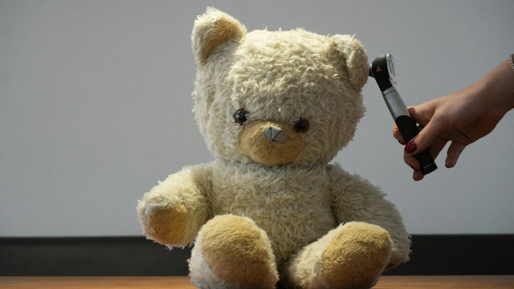 Hand holding an otoscope to a teddy bear's ear, illustrating an ear examination