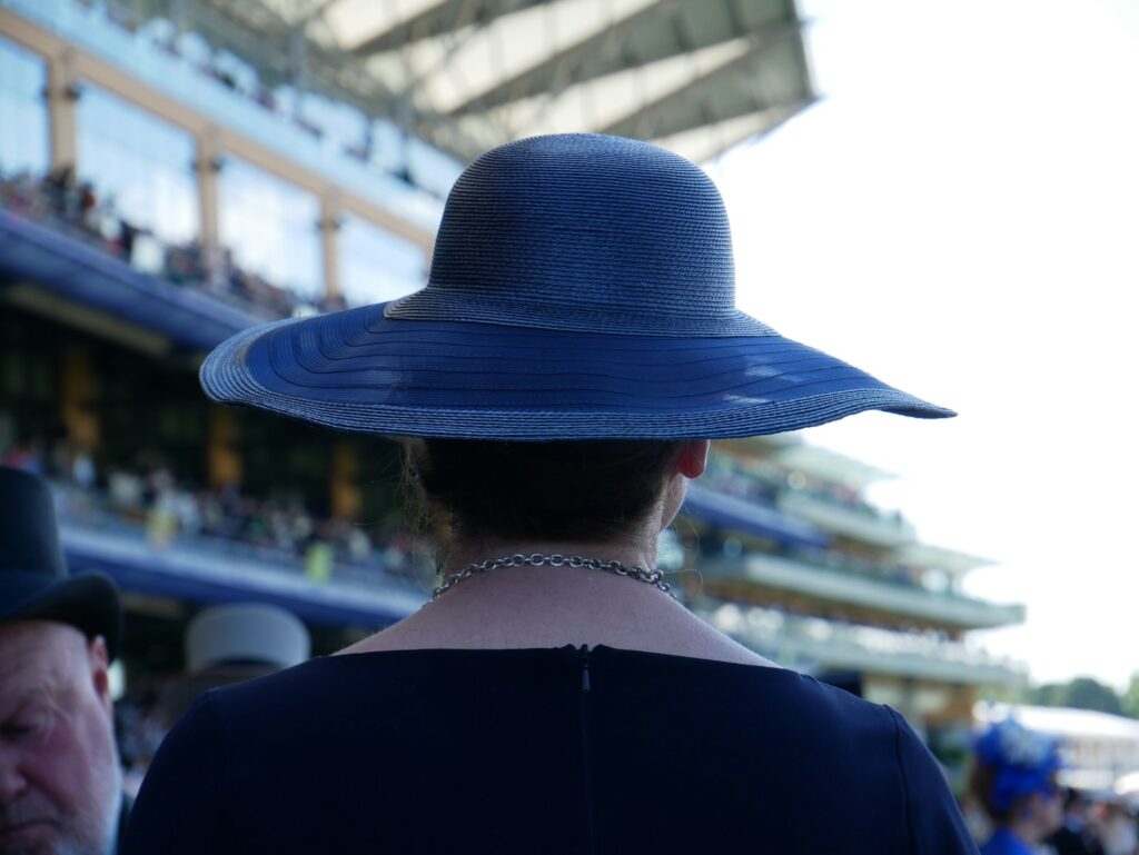Woman in a blue hat at a race meeting, showing a Royal Ascot hat style