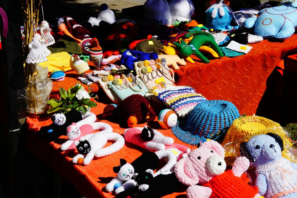 Handmade crochet toys and hats displayed on an orange tablecloth at an outdoor market
