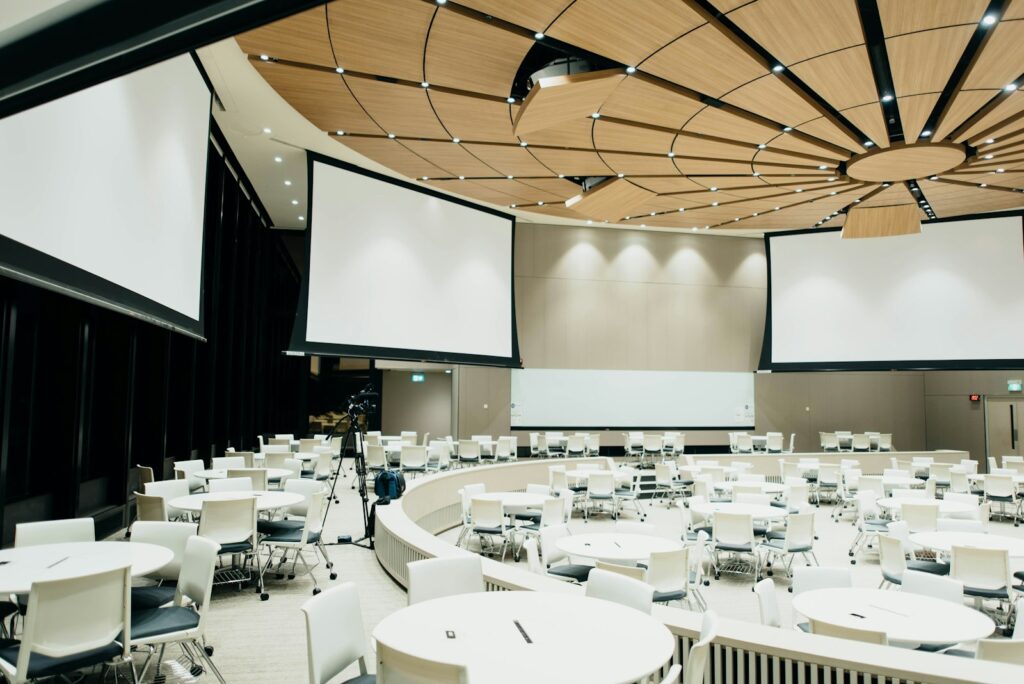 Large conference room with round tables, white chairs and three projection screens, a typical corporate venue layout
