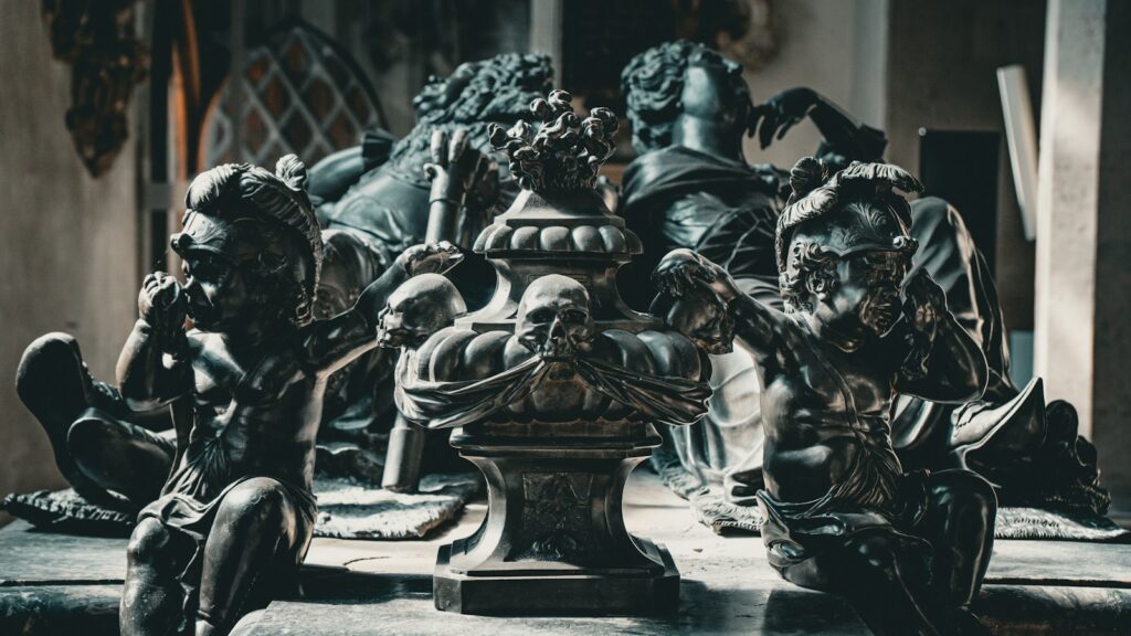 Two dark bronze cherub statues flanking a central urn decorated with a skull