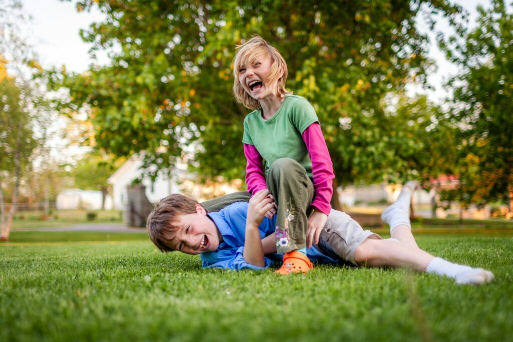 Two children laughing while playing together on grass, reflecting the bond between siblings in foster care