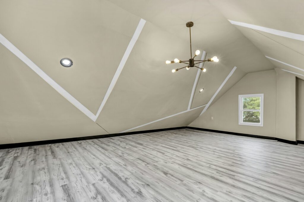 Empty converted attic room with sloped ceiling, grey wood-effect flooring and a brass sputnik-style chandelier